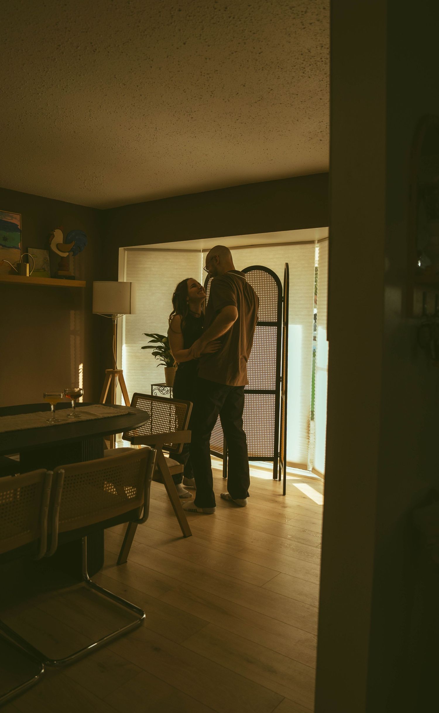 Couple sharing intimate embrace in warmly lit apartment living room at golden hour.