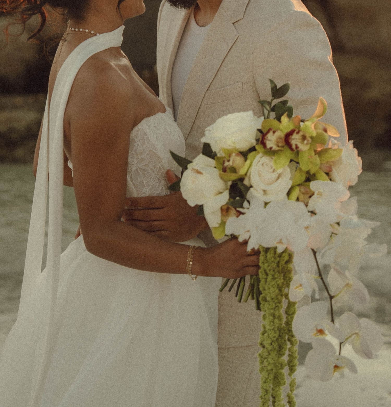 Bride and groom embracing with a beautiful white and green orchid wedding bouquet at their outdoor ceremony.