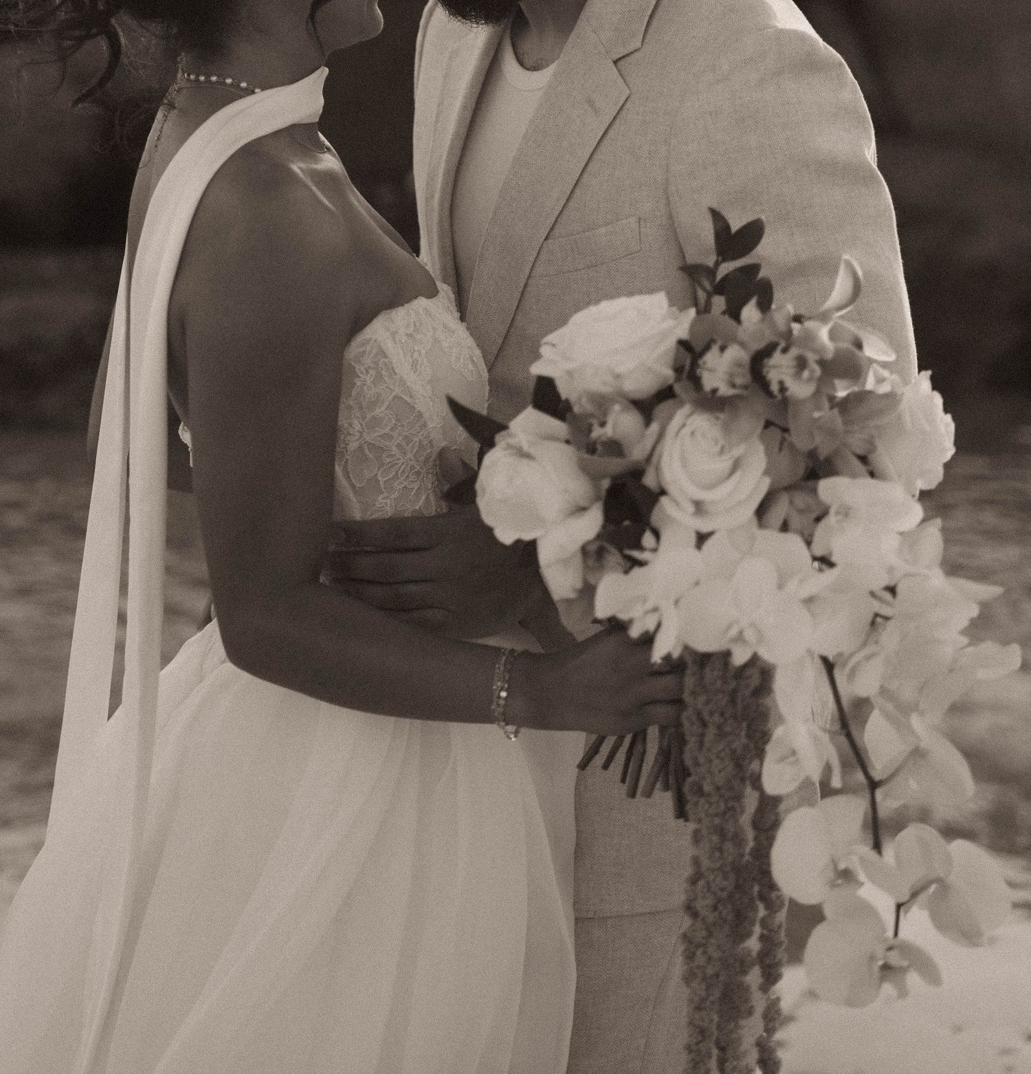 Romantic sepia-toned portrait of bride and groom embracing, bride holding lush white floral bouquet.