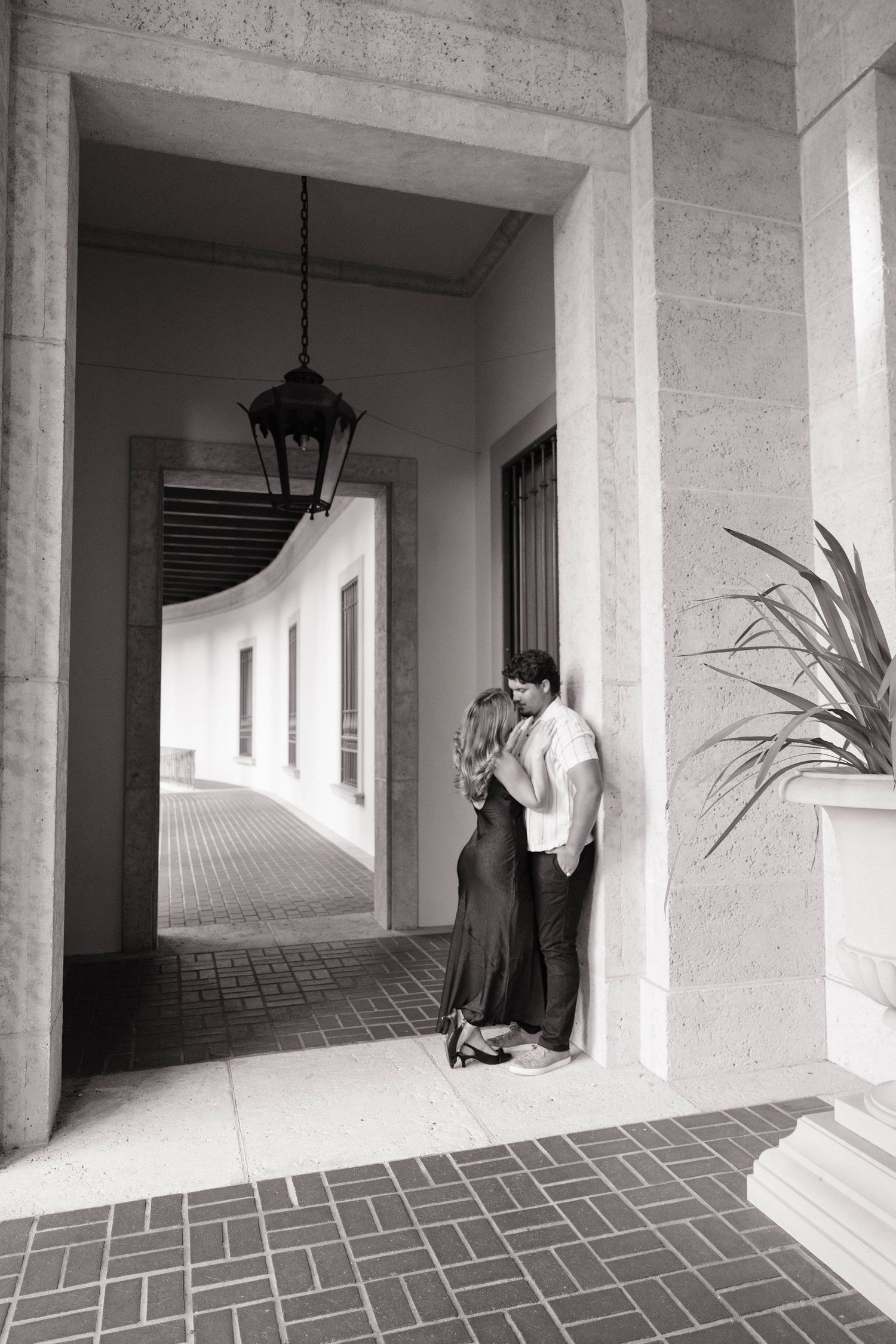 Black and white photo of a couple sharing a kiss in a grand stone archway corridor.