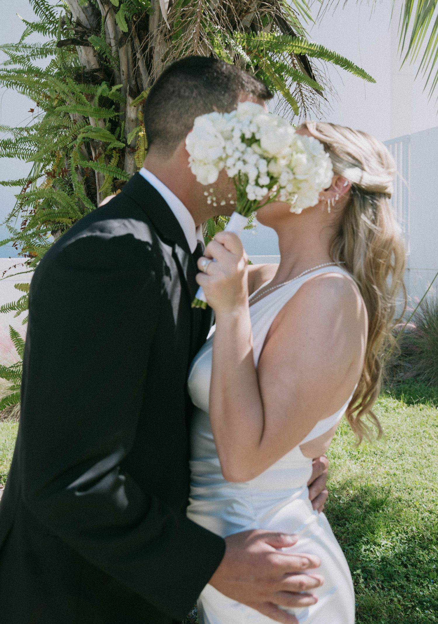 Bride and groom sharing a kiss hidden behind white hydrangea and baby's breath bridal bouquet.