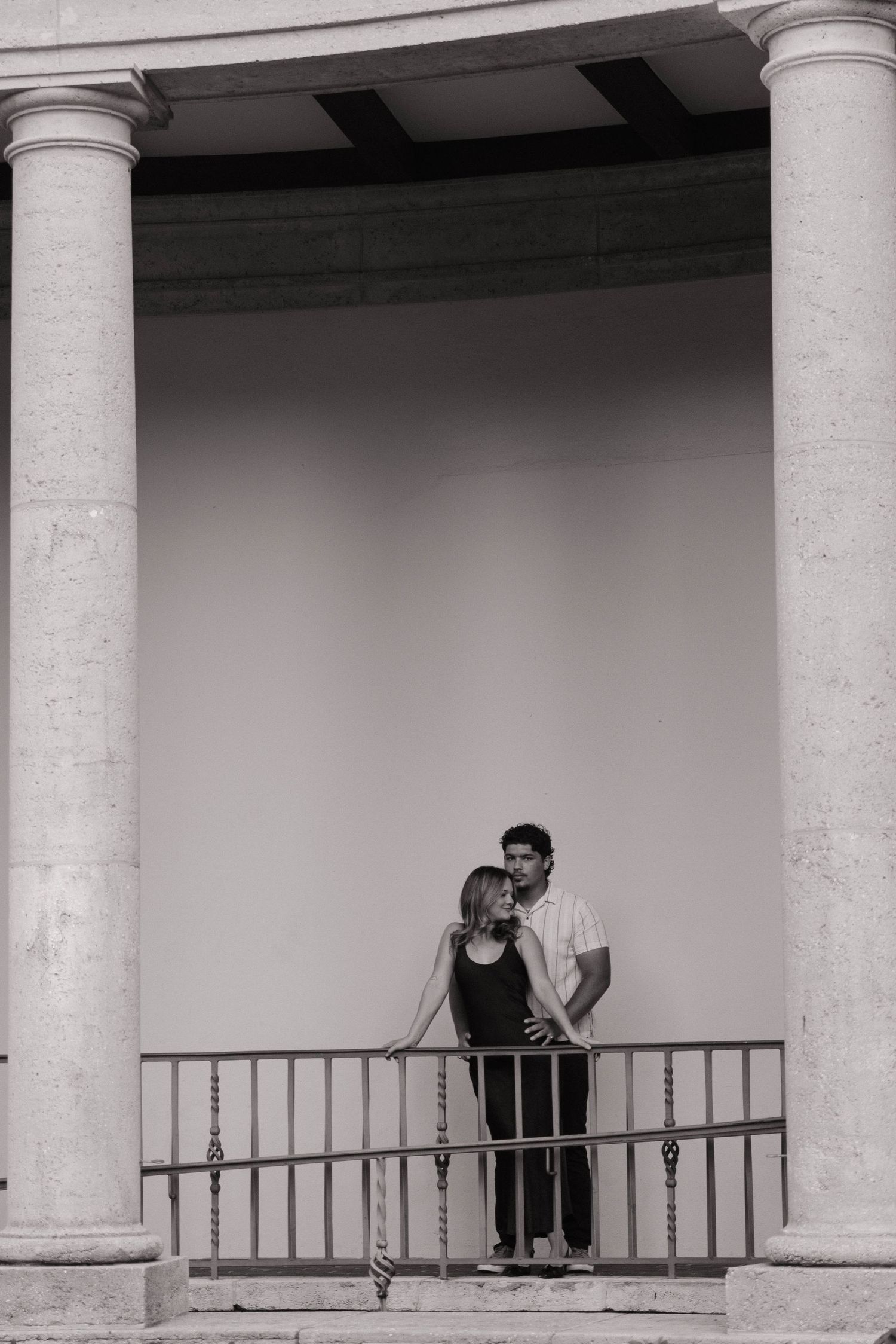 Couple posing between grand columns on balcony in black and white engagement photo.