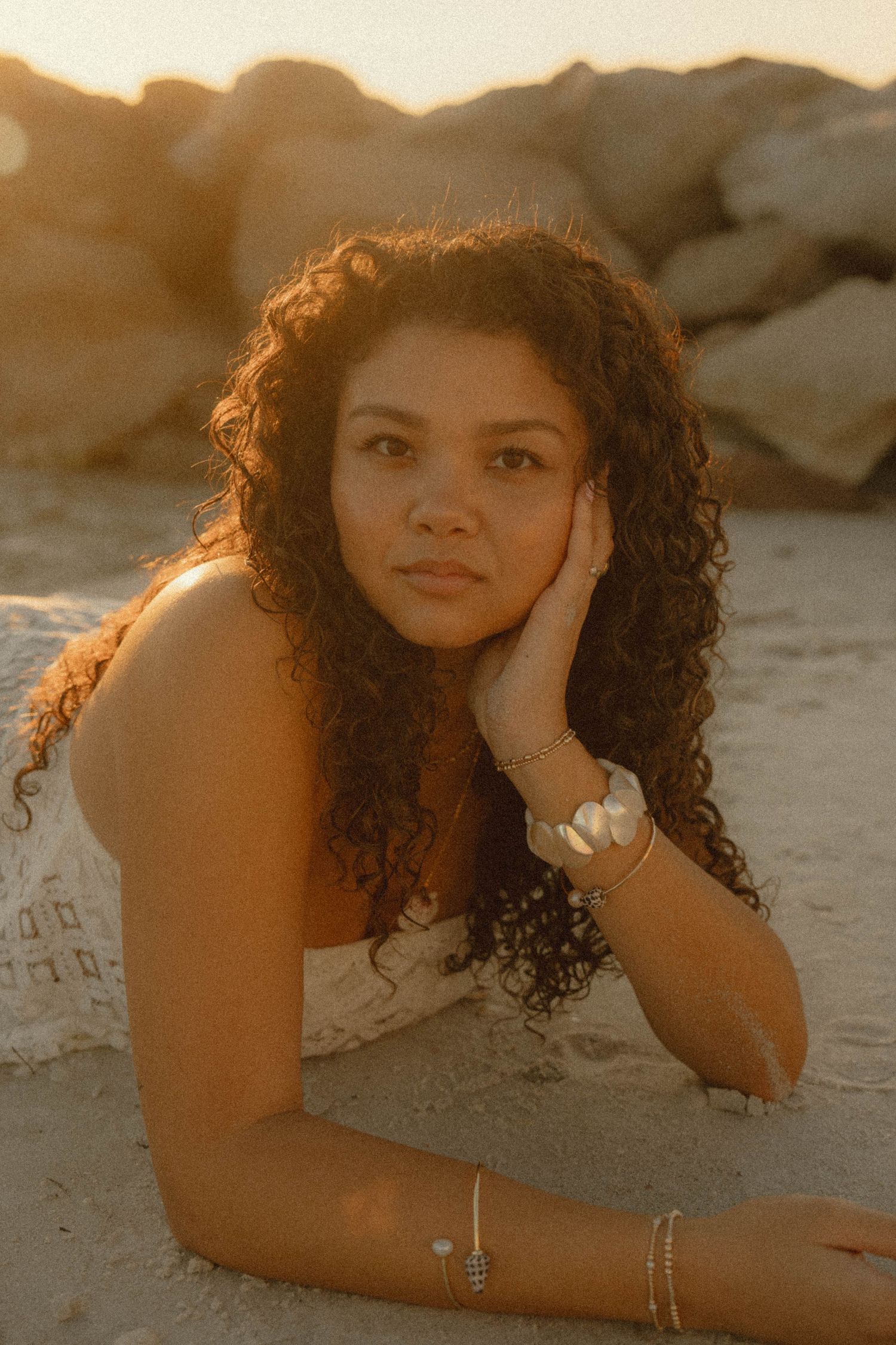 Young woman with curly hair resting on sandy beach at golden hour sunset.