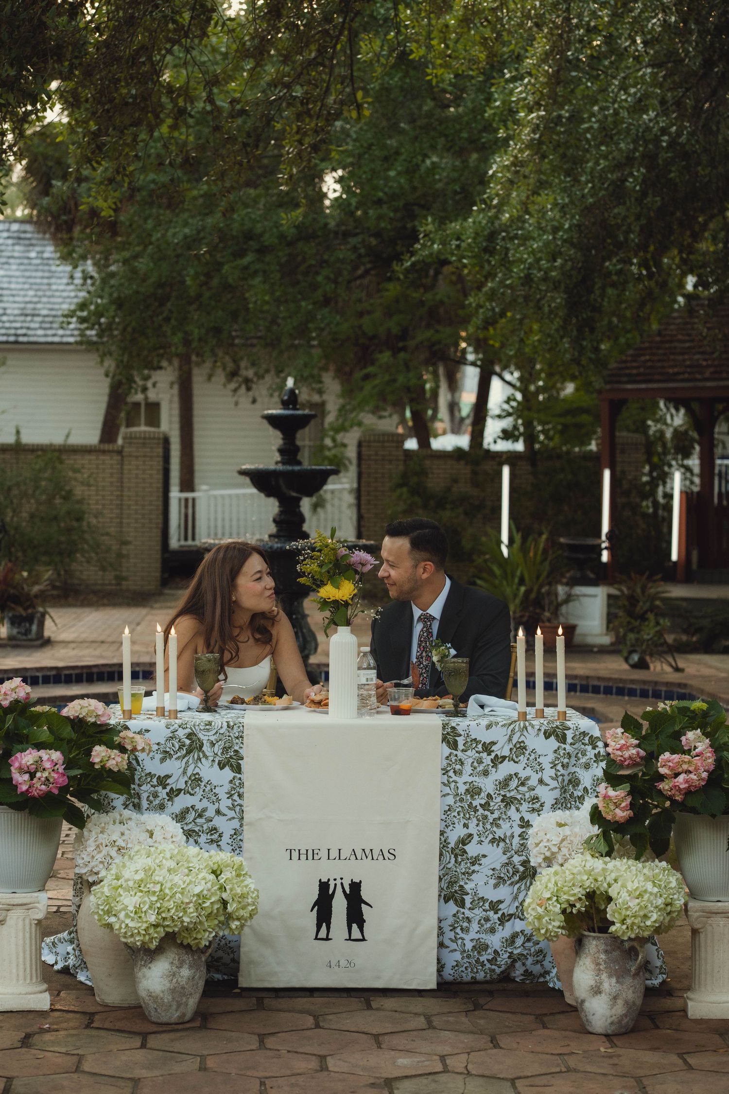 Bride and groom share a romantic moment at their sweetheart table decorated with hydrangeas and a custom The Llamas banner.