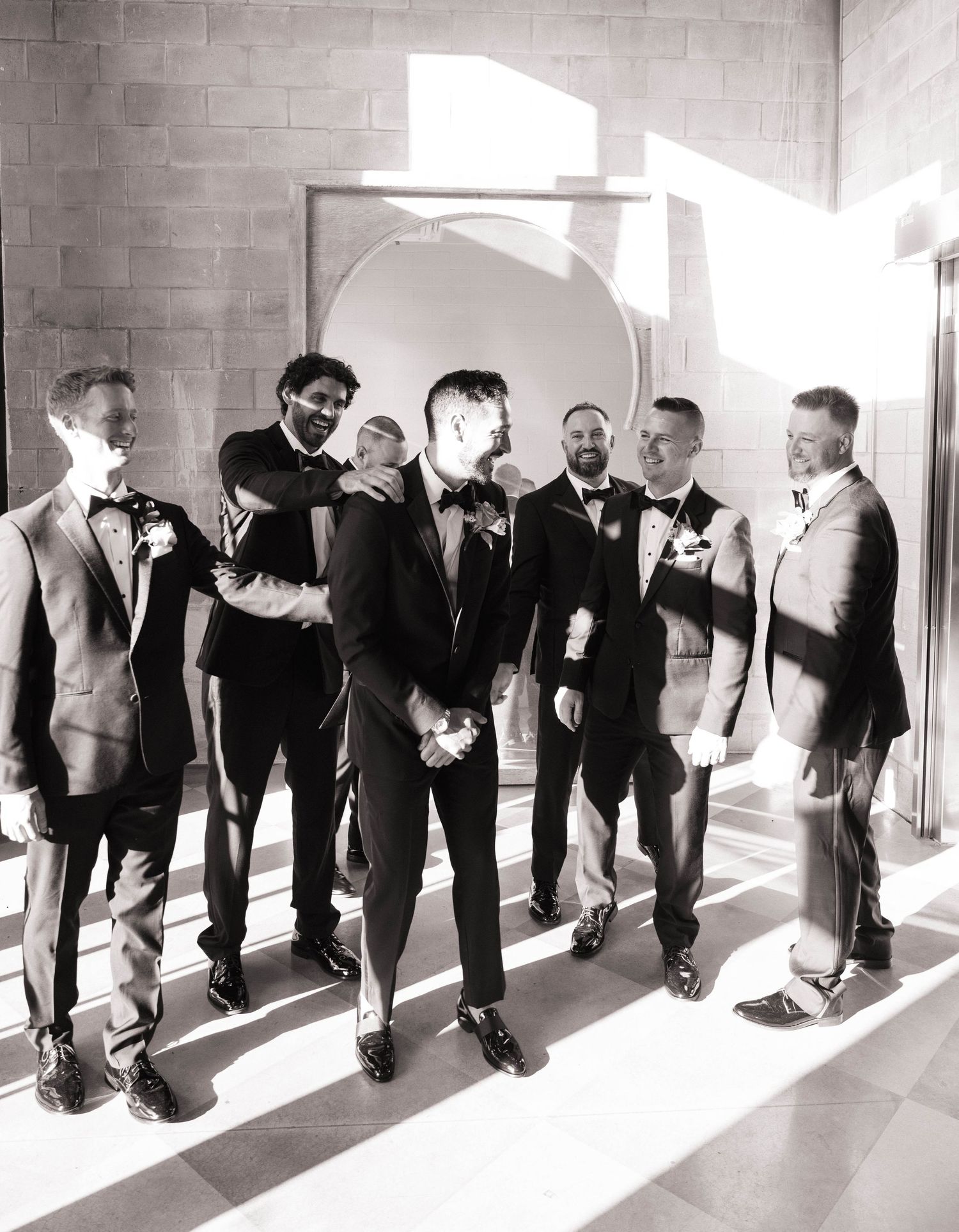 Groom and groomsmen laughing together in black and white photo before wedding ceremony.