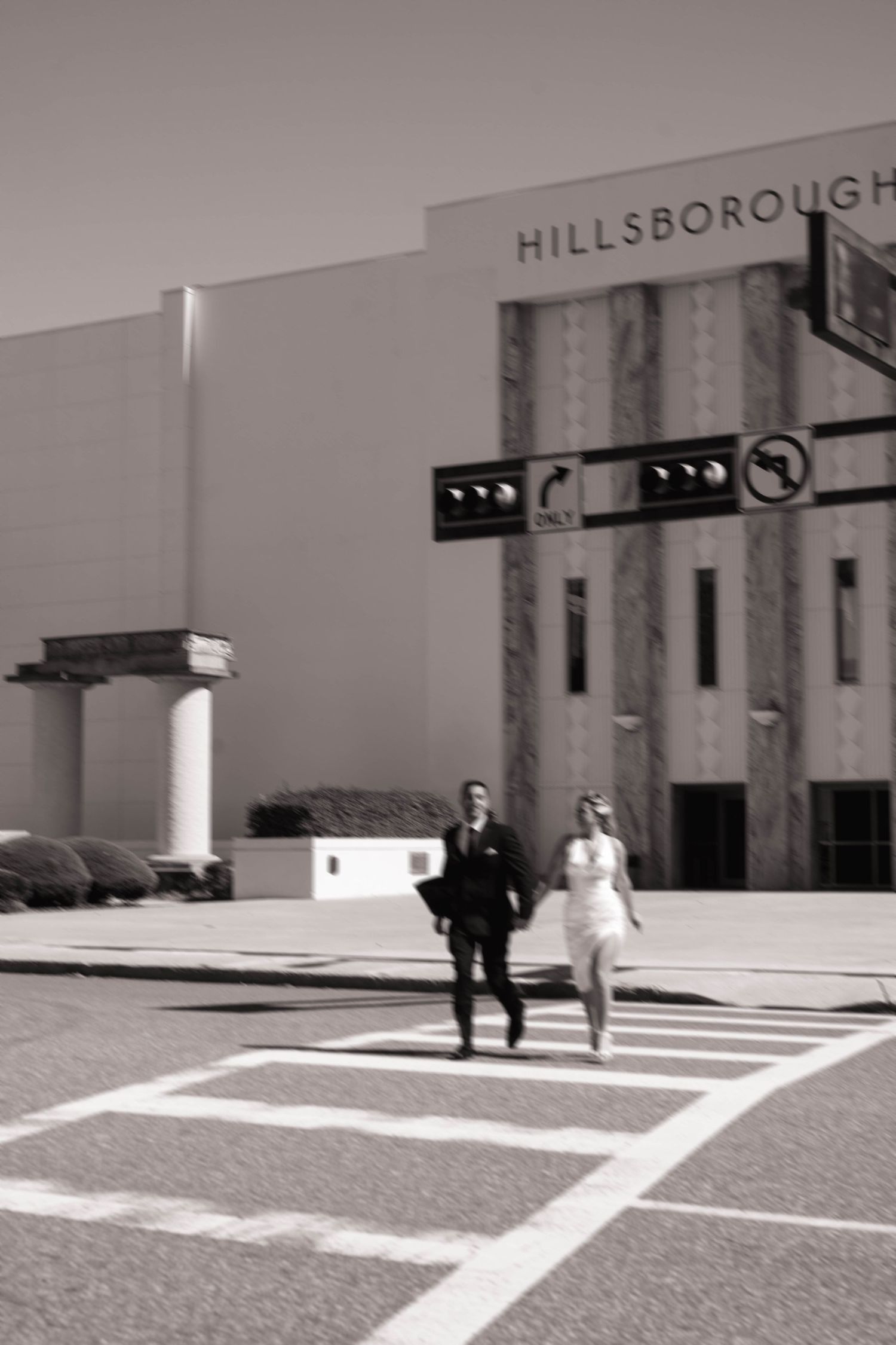 Black and white photo of wedding couple crossing street in front of Hillsborough building.