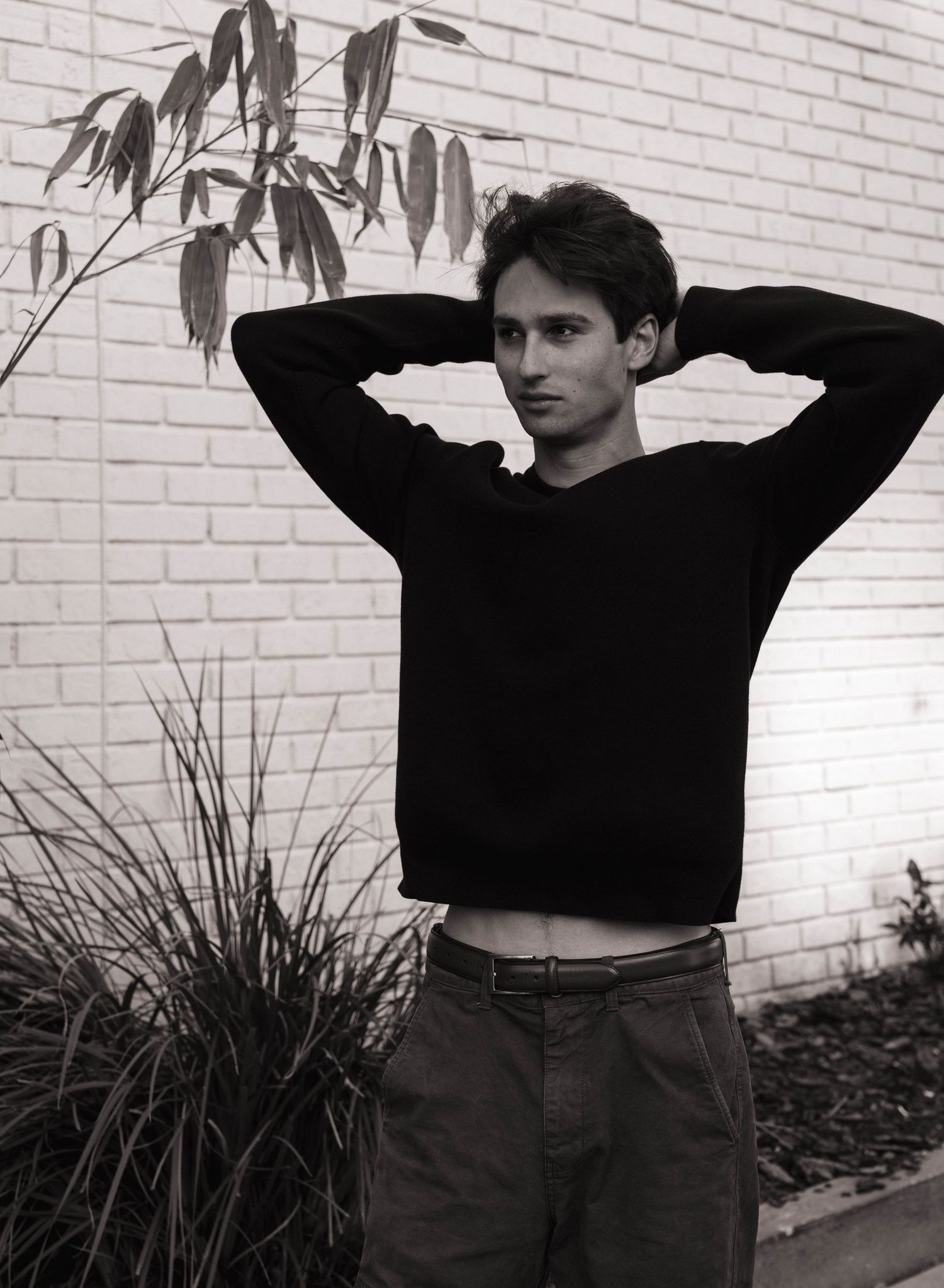 Black and white photo of a young man in a black sweater posing with hands behind his head.