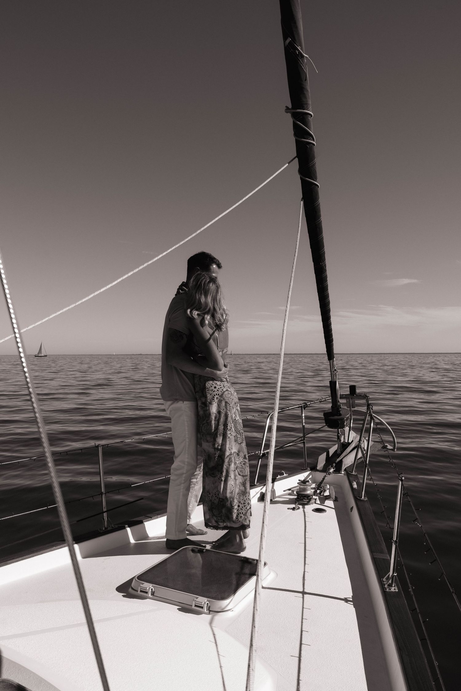Romantic couple embracing on sailboat bow overlooking calm ocean in black and white.