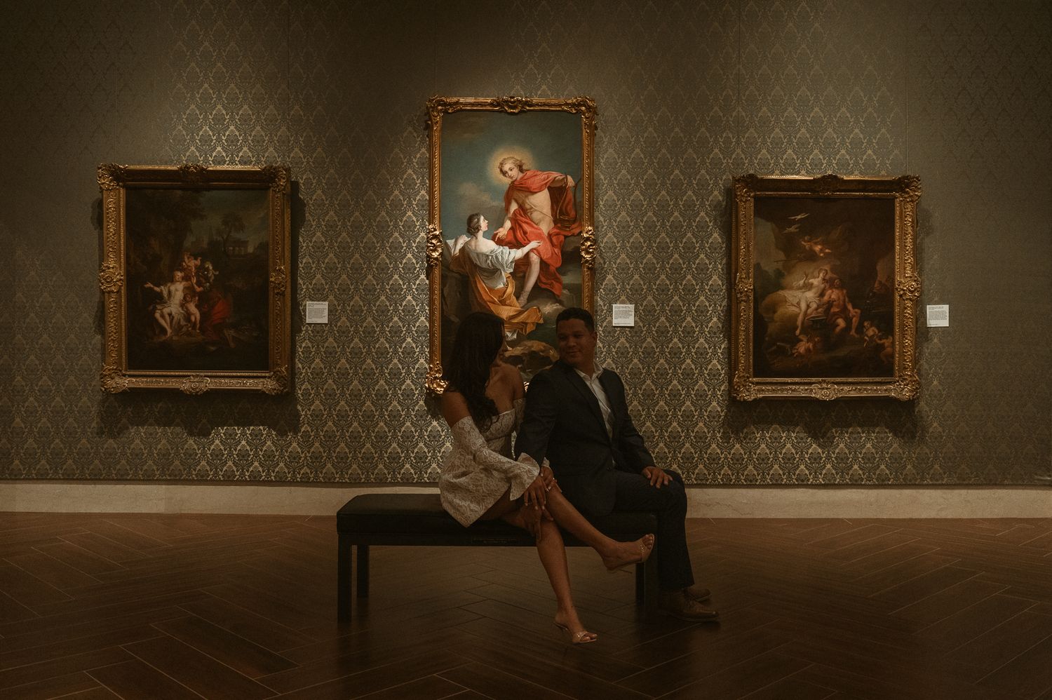 Couple posing romantically in an art museum gallery with classical oil paintings on teal damask walls.
