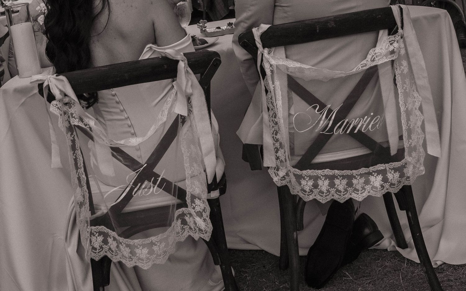 Black and white photo of wedding chairs decorated with lace signs reading Just Married.