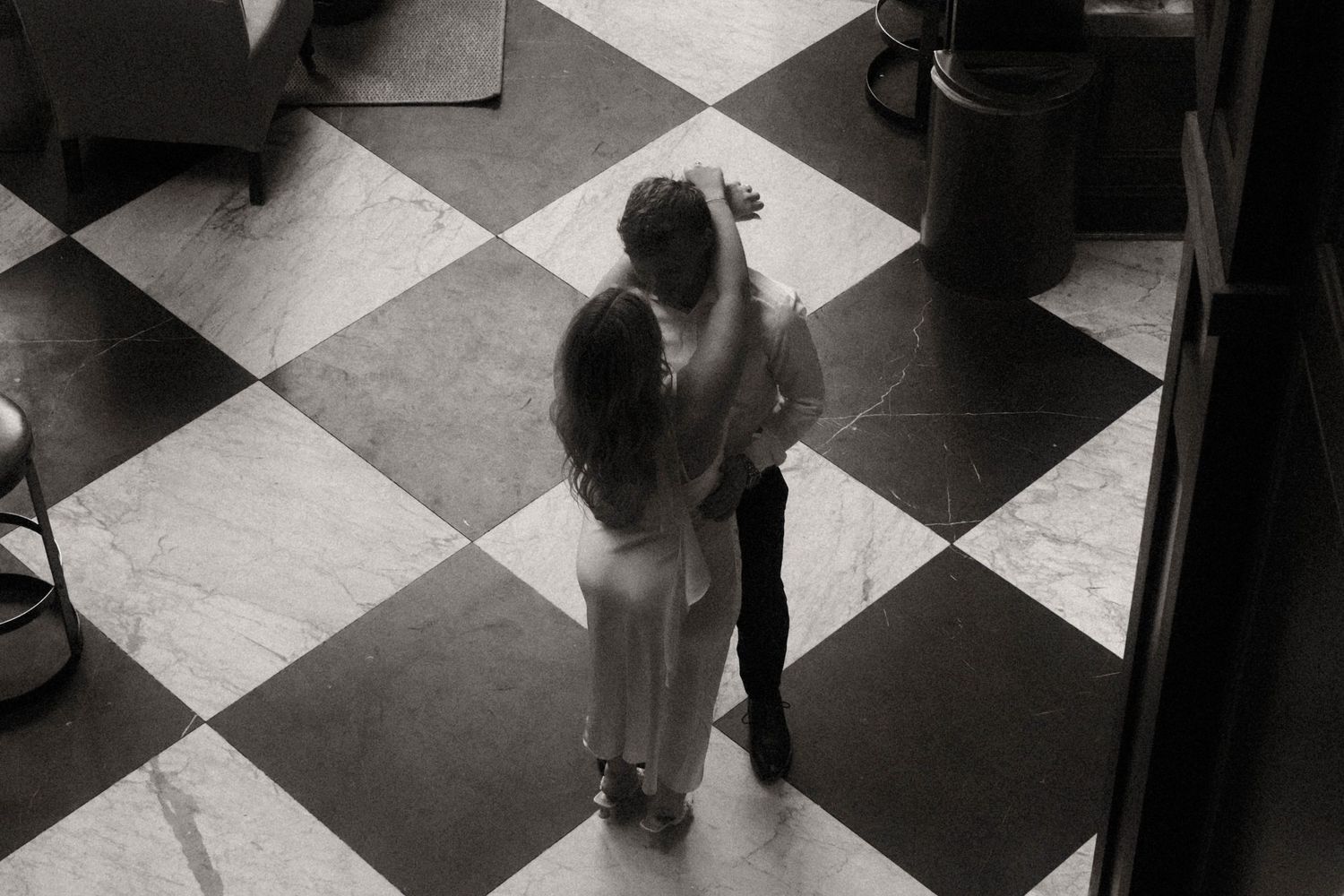 Aerial black and white photo of couple embracing on classic checkered tile floor.
