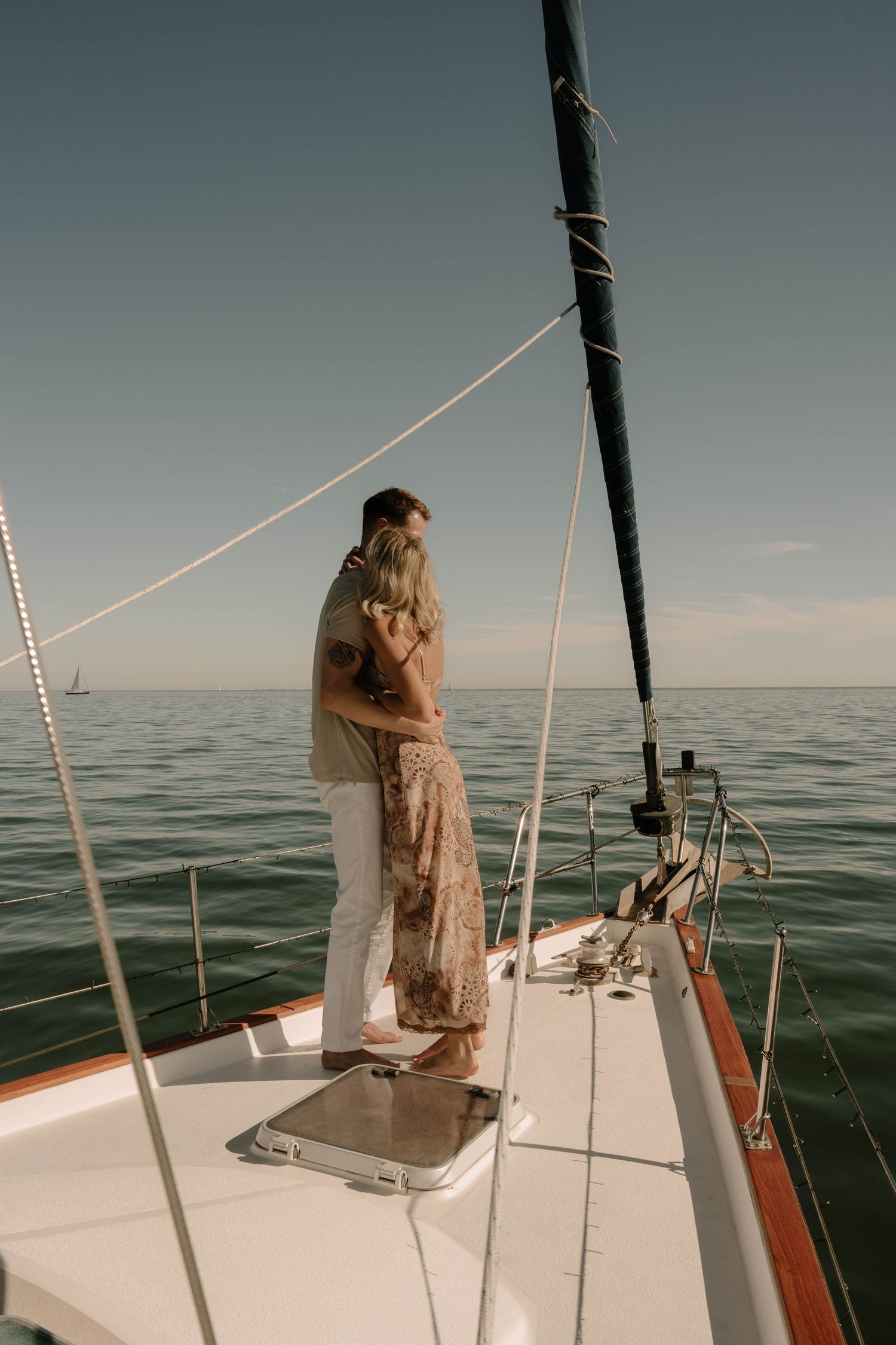 Couple embracing on the bow of a sailboat with calm open ocean in background.