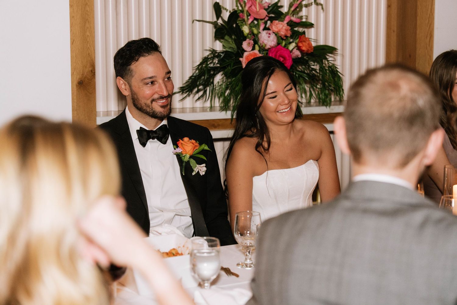 Bride and groom smile and laugh together at the head table during their elegant wedding reception dinner.
