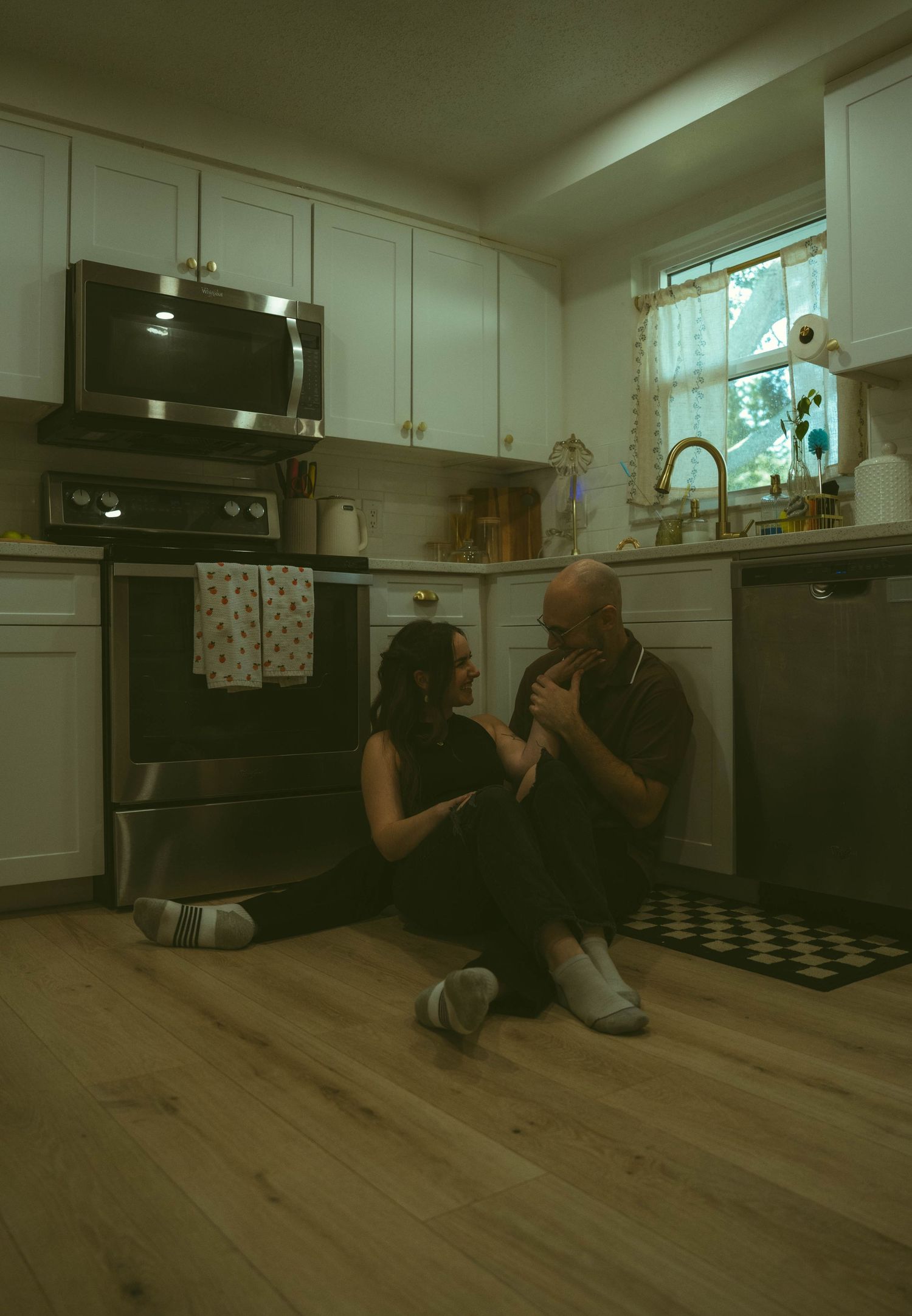 Couple sitting on kitchen floor sharing an intimate moment near the stove in a cozy home.