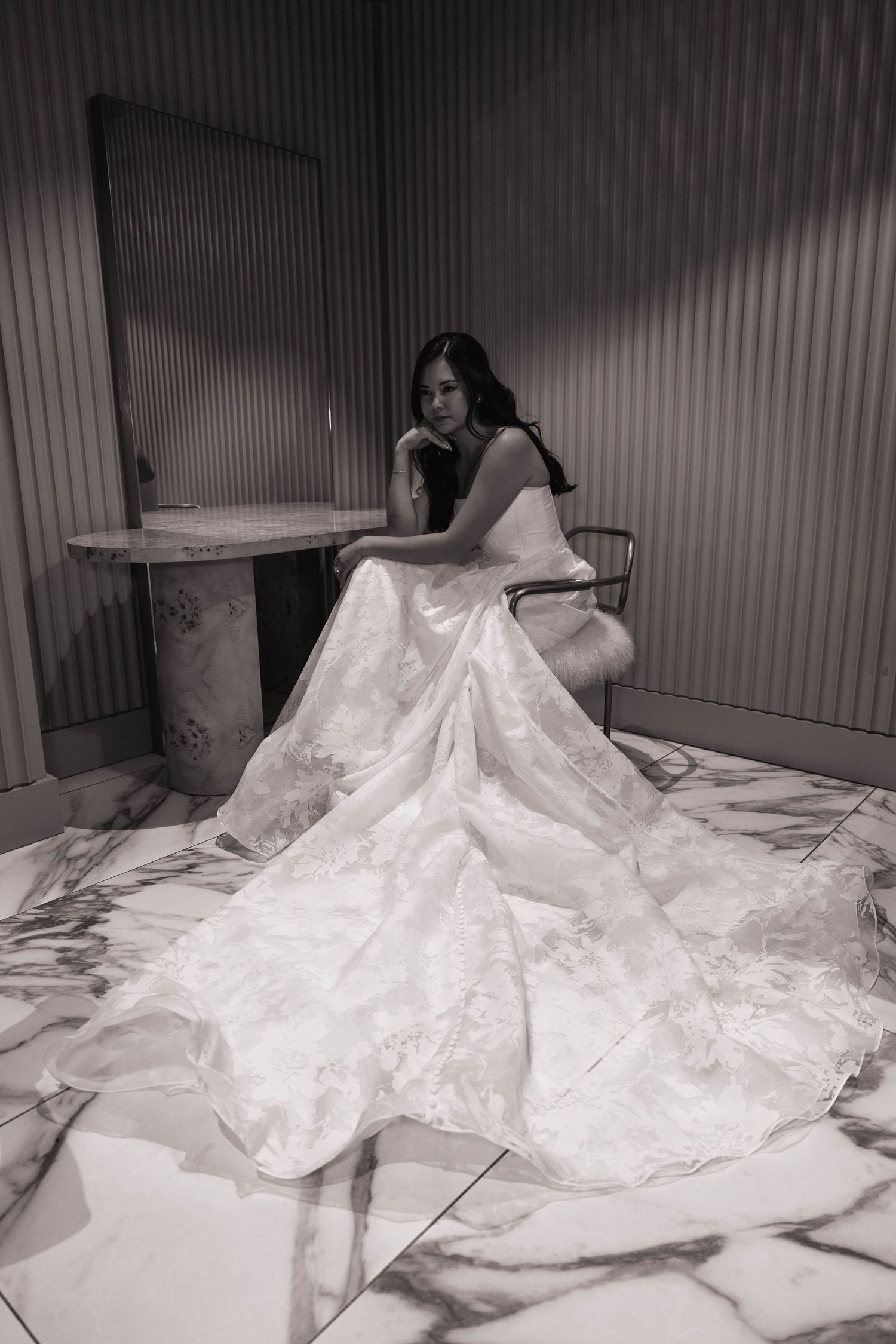 Black and white artistic portrait of a bride in a dramatic lace gown seated on a marble floor.
