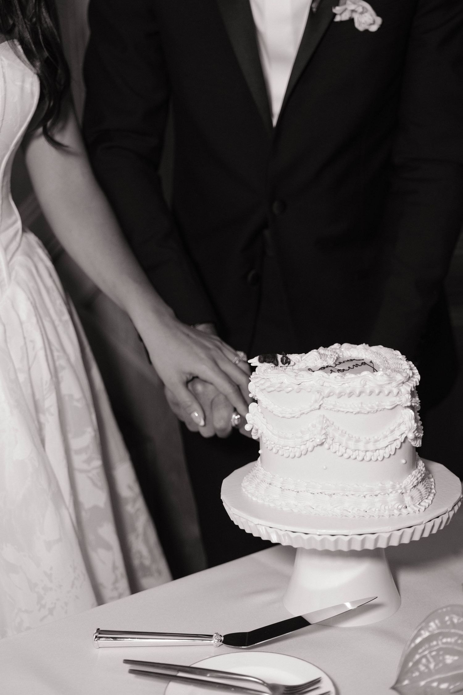 Black and white photo of bride and groom cutting a two-tier white wedding cake at their reception.