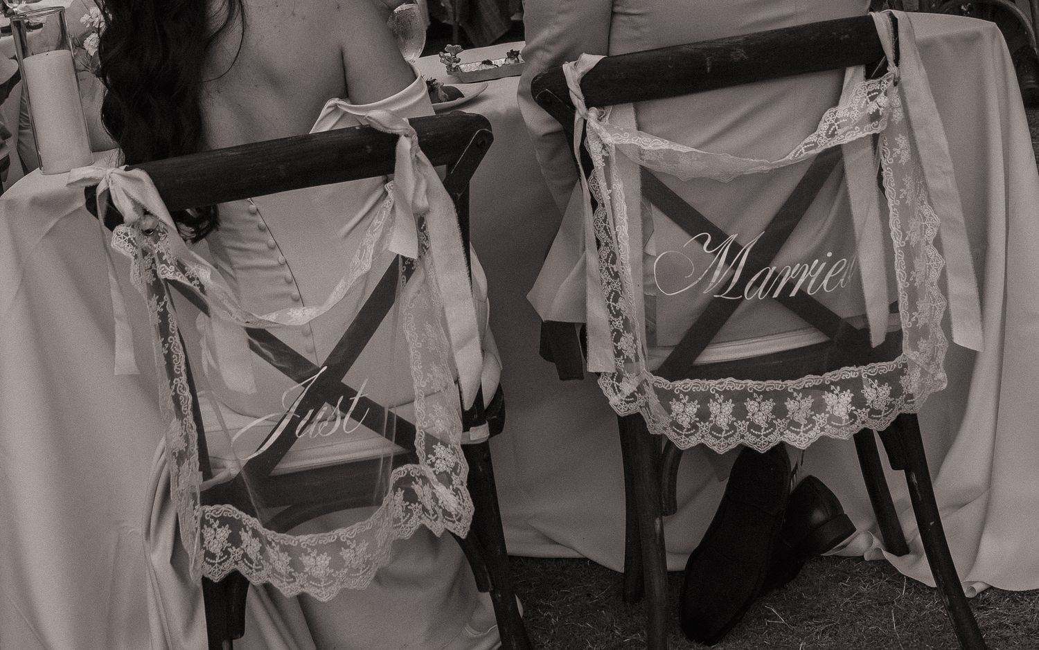 Black and white photo of wedding chairs decorated with lace and signs reading Just Married at a reception venue.
