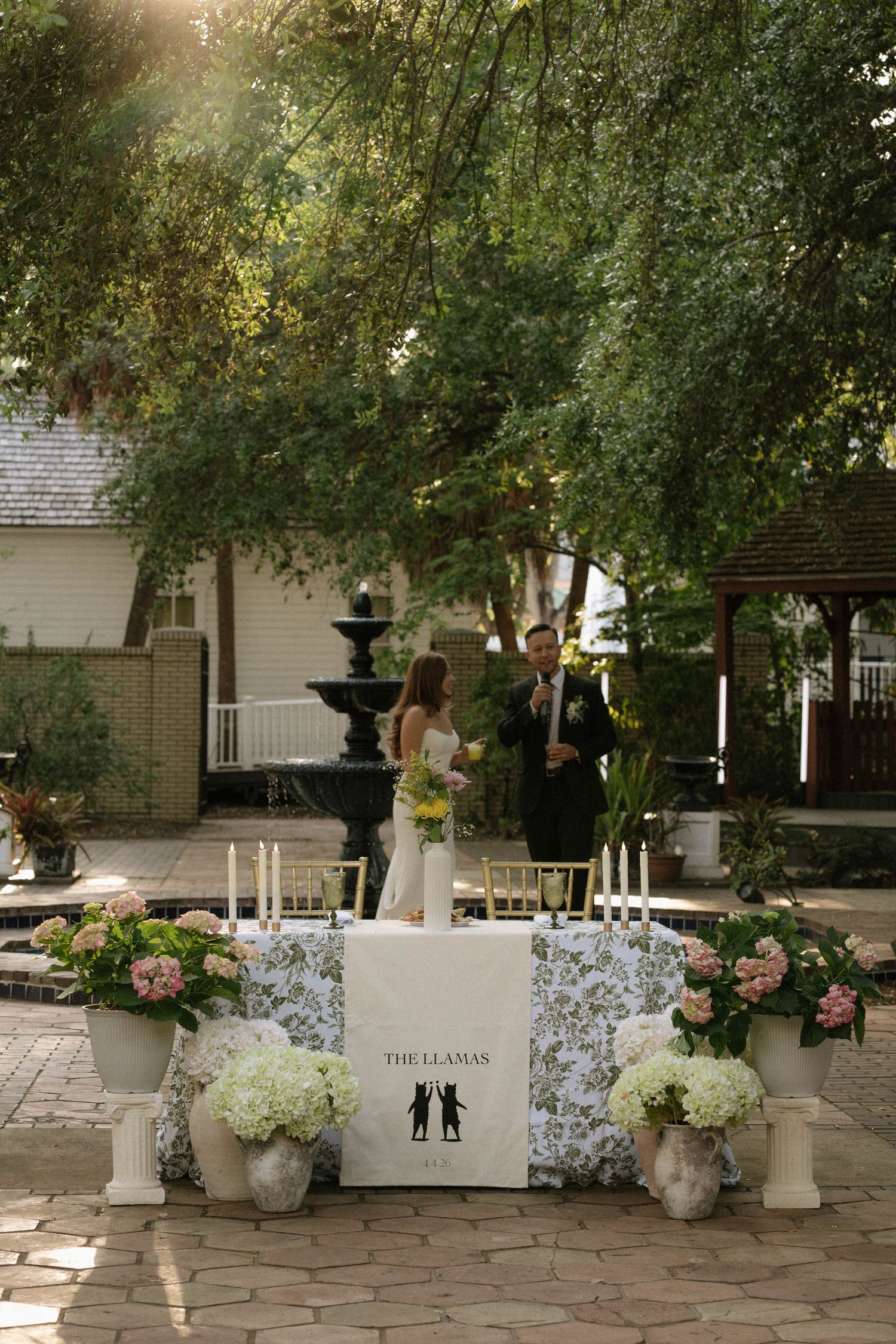 Sweetheart table decorated with hydrangeas and candles with couple in background at outdoor wedding reception.