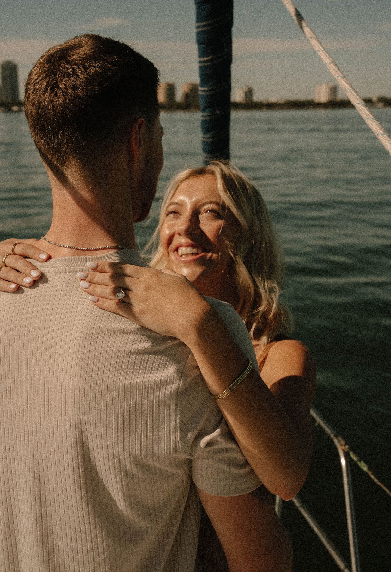 Happy engagement on sailboat with waterfront skyline backdrop during golden hour engagement photo.
