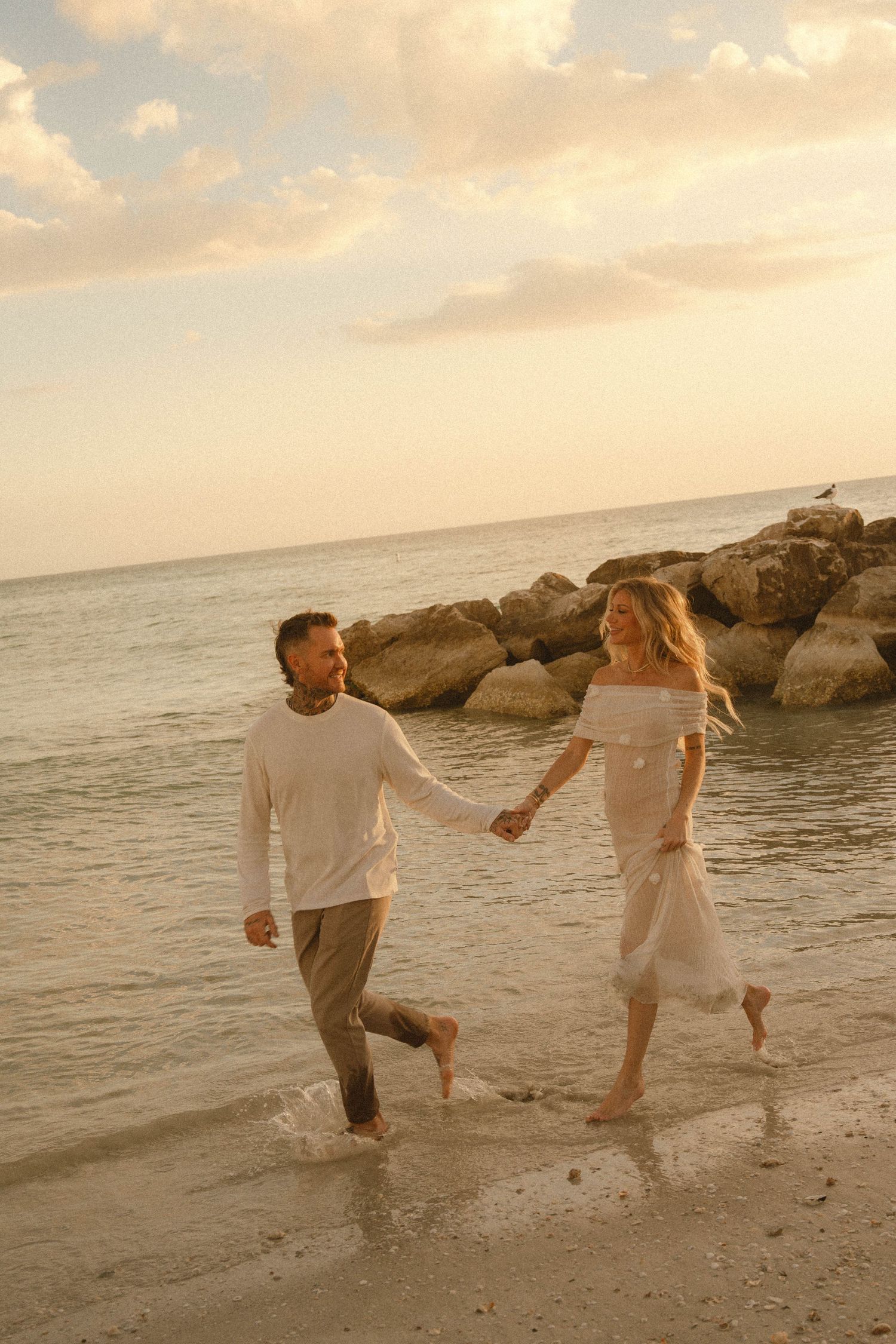 Happy couple holding hands and running along a sandy beach at golden hour sunset.