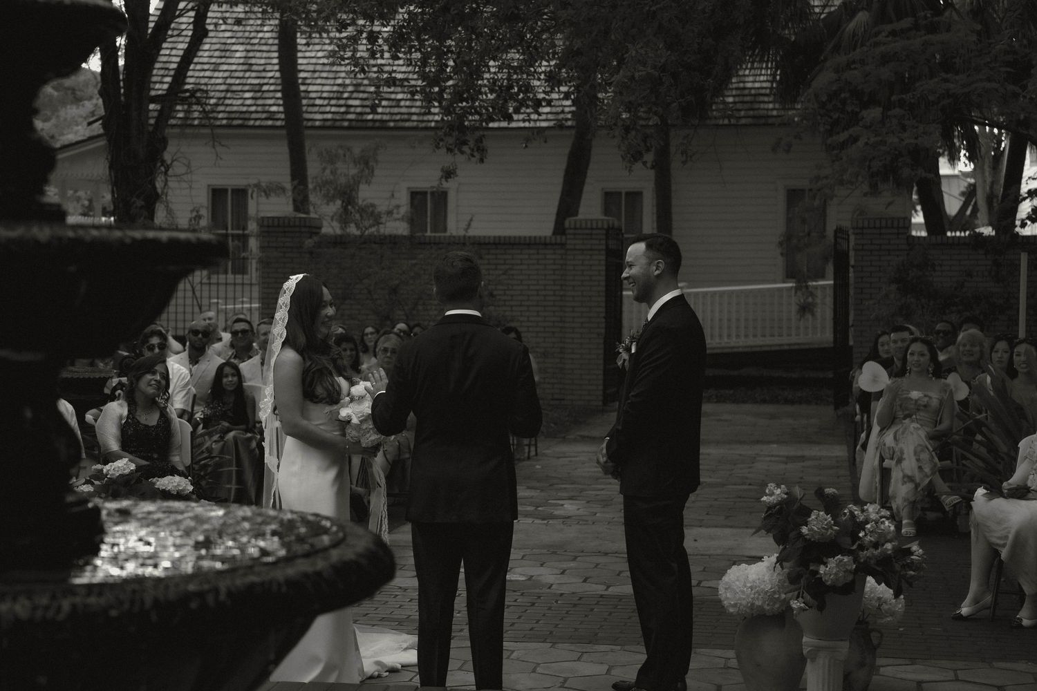 Bride and groom standing at outdoor fountain during intimate black and white ceremony.