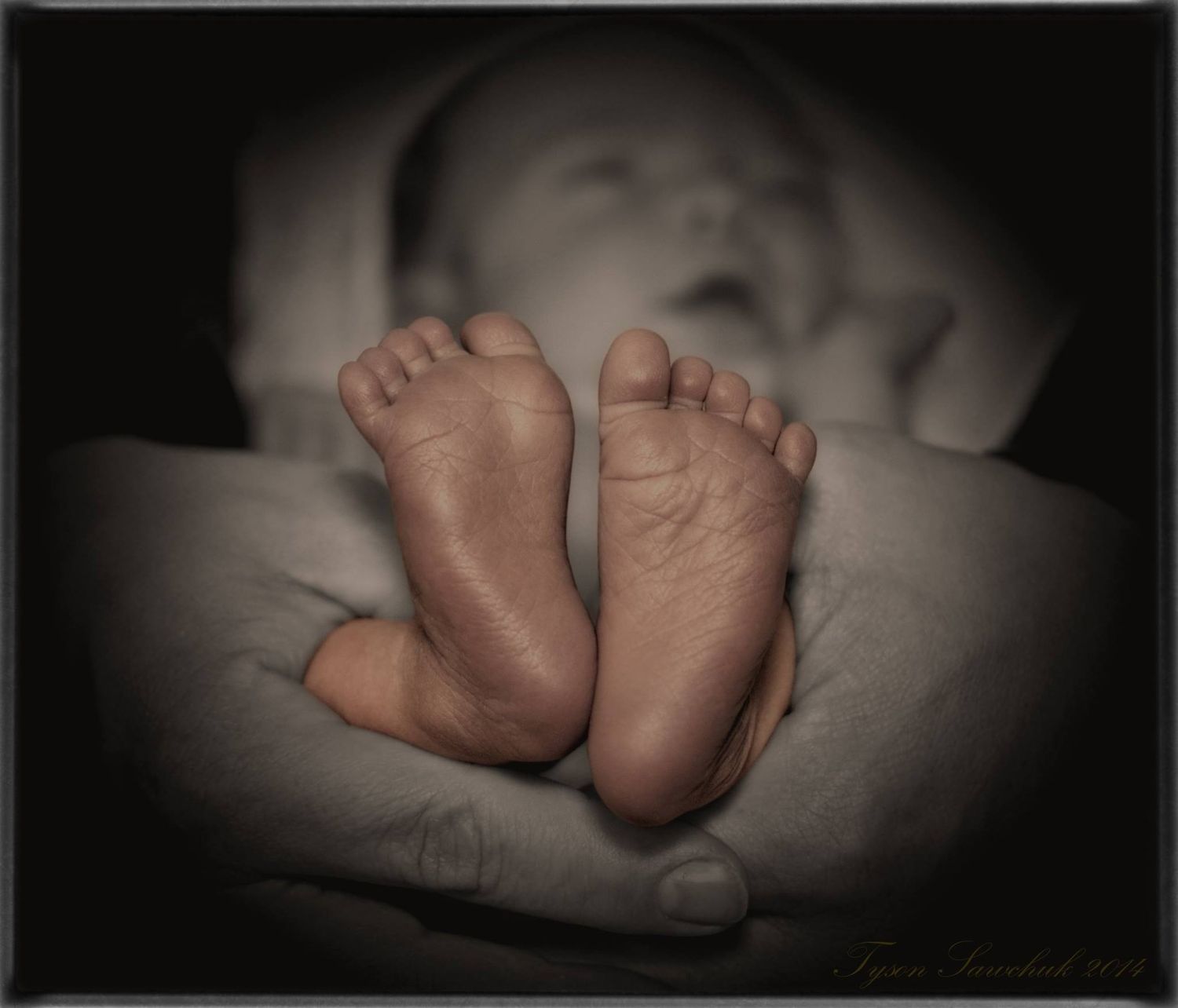 A close-up black and white photo of a newborn baby's tiny feet cradled in adult hands.