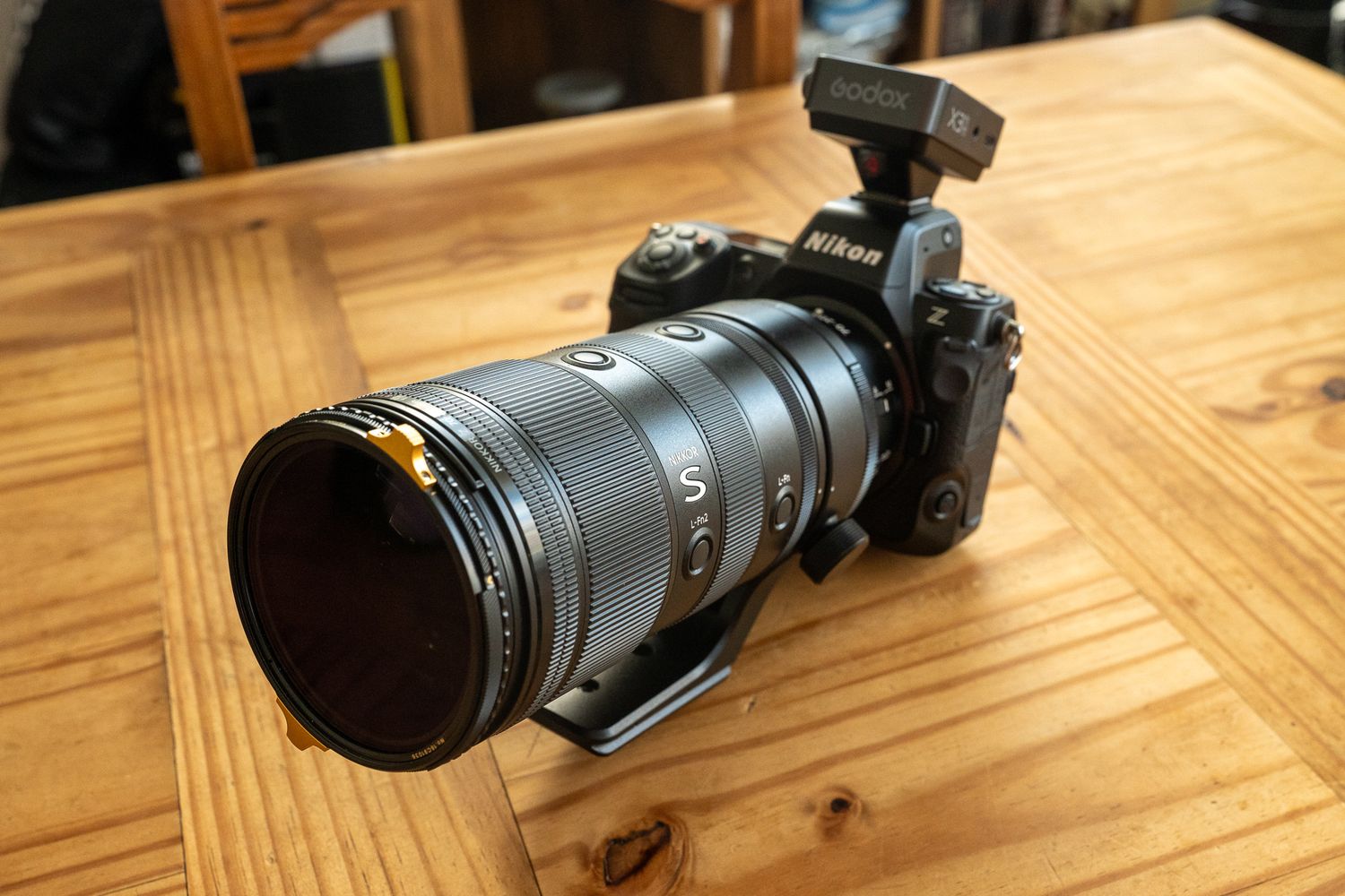 Nikon mirrorless camera with a long telephoto lens mounted on a tripod collar, placed on a wooden table.