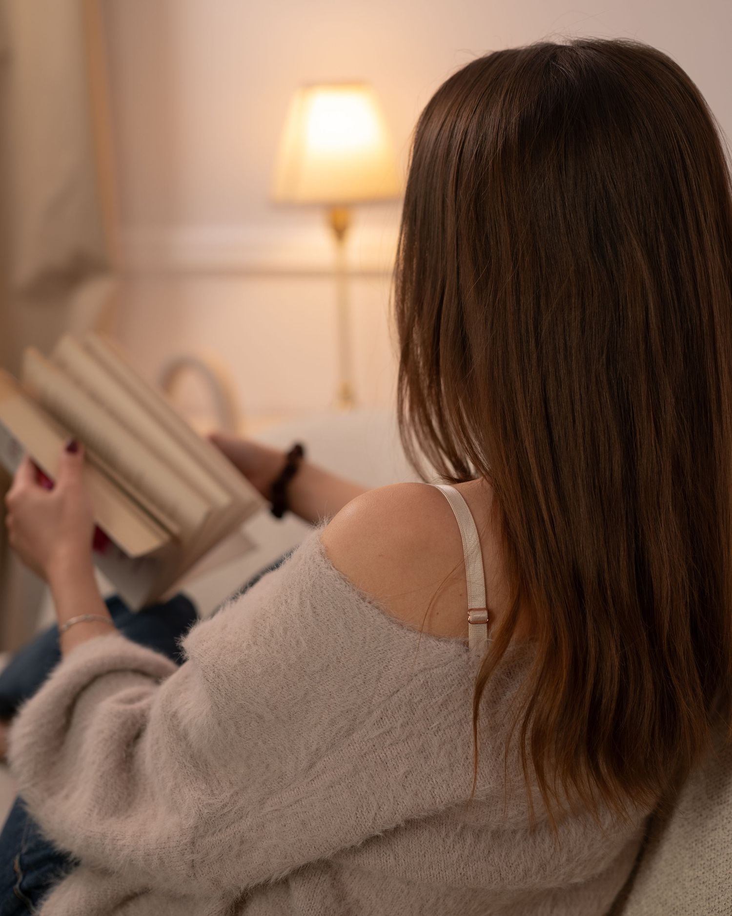 Kobieta czytająca książkę na sofie w przytulnym pokoju. Naturalna, ciepła sesja zdjęciowa lifestyle.