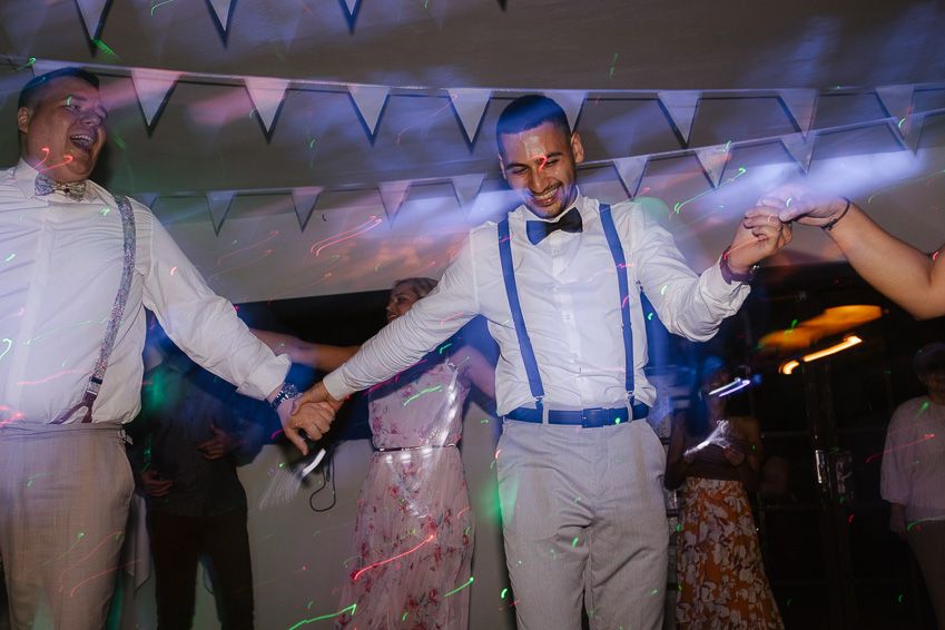 Groom dances joyfully with guests wearing suspenders at lively wedding reception party.
