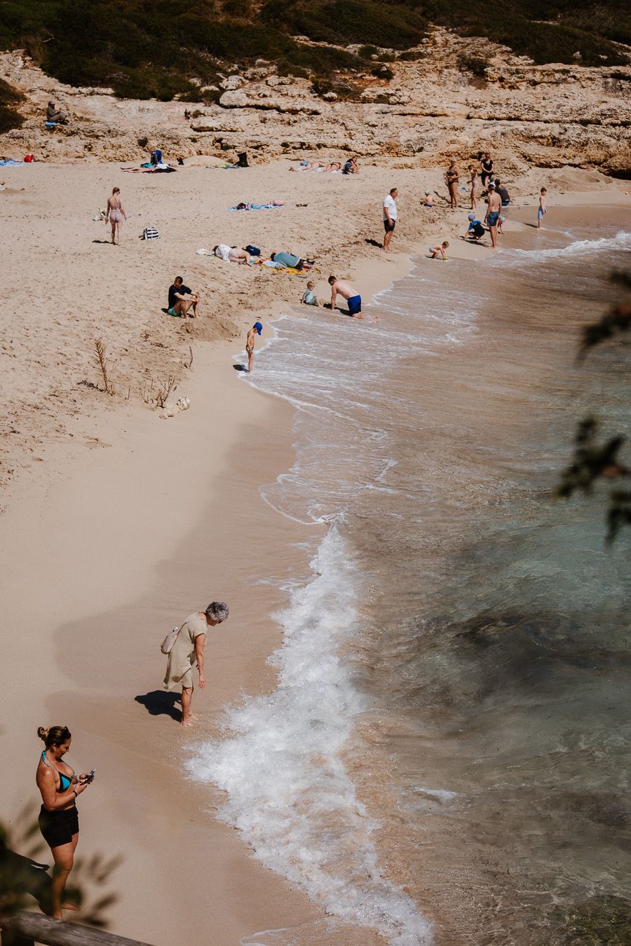 Aerial view of sandy cove beach with waves and sunbathers on a warm sunny day.