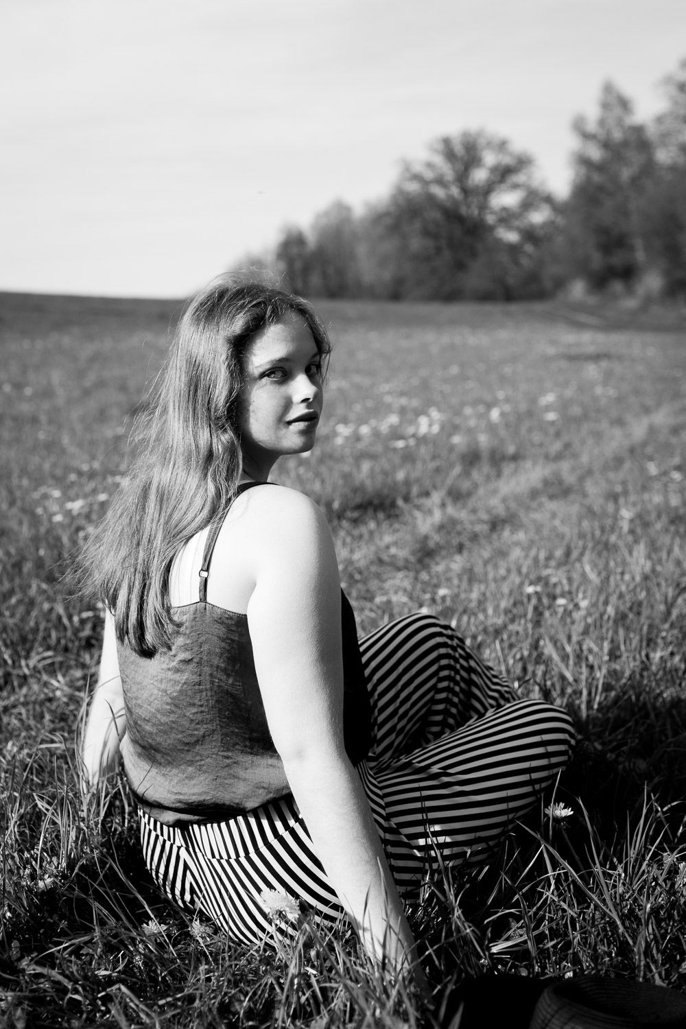 Black and white portrait of young woman sitting in a grassy field outdoors.