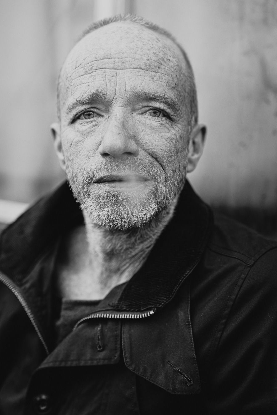 Black and white portrait of an older bald man with a short beard wearing a dark jacket, looking directly at the camera.