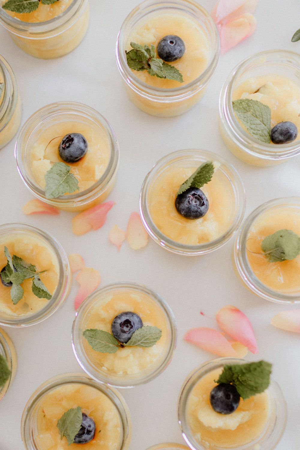 Overhead view of individual dessert cups with yellow mousse, blueberries, and mint leaves.