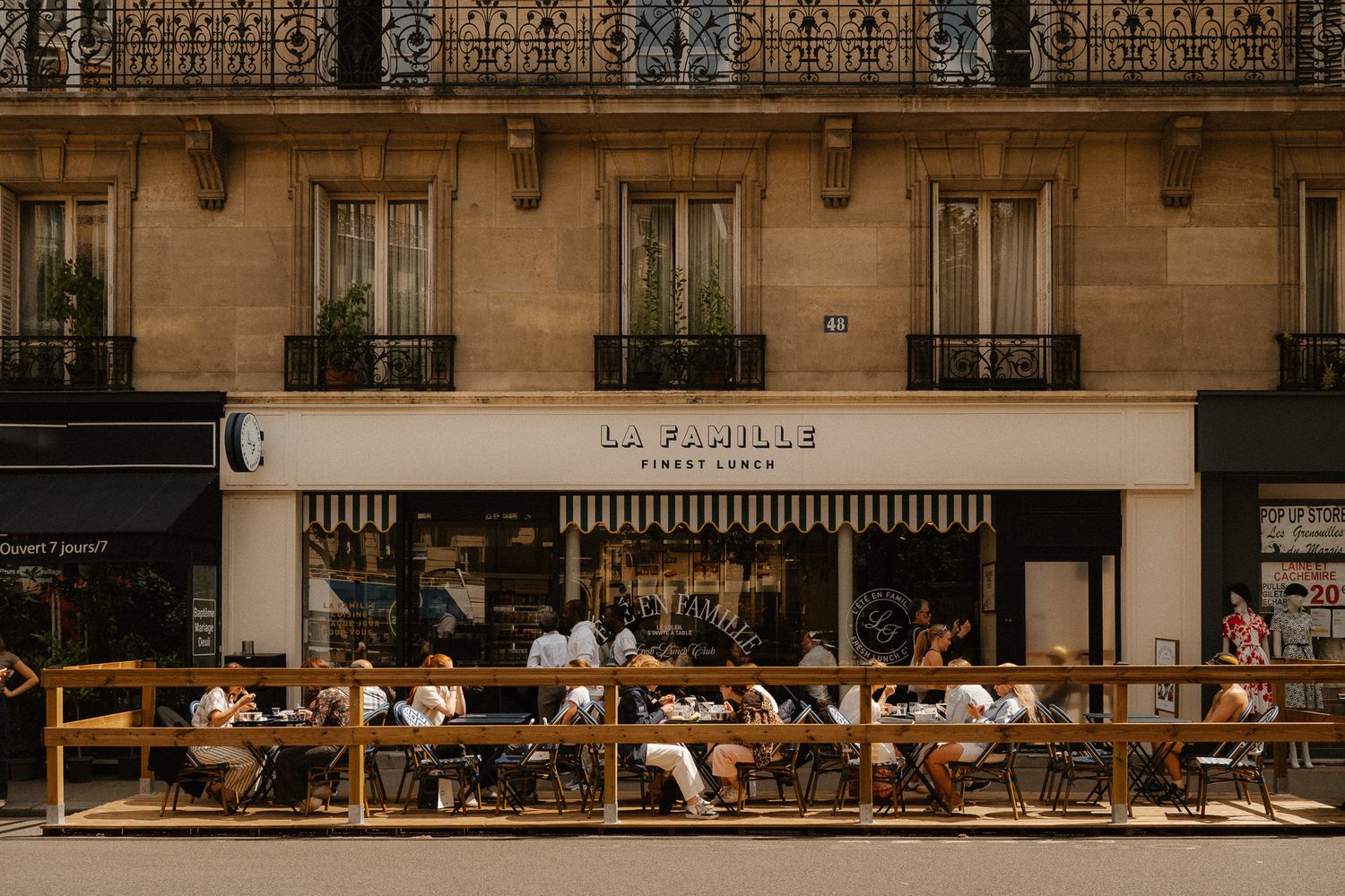 Parisian cafe terrace with diners seated outside La Famille restaurant on a classic Haussmann boulevard.