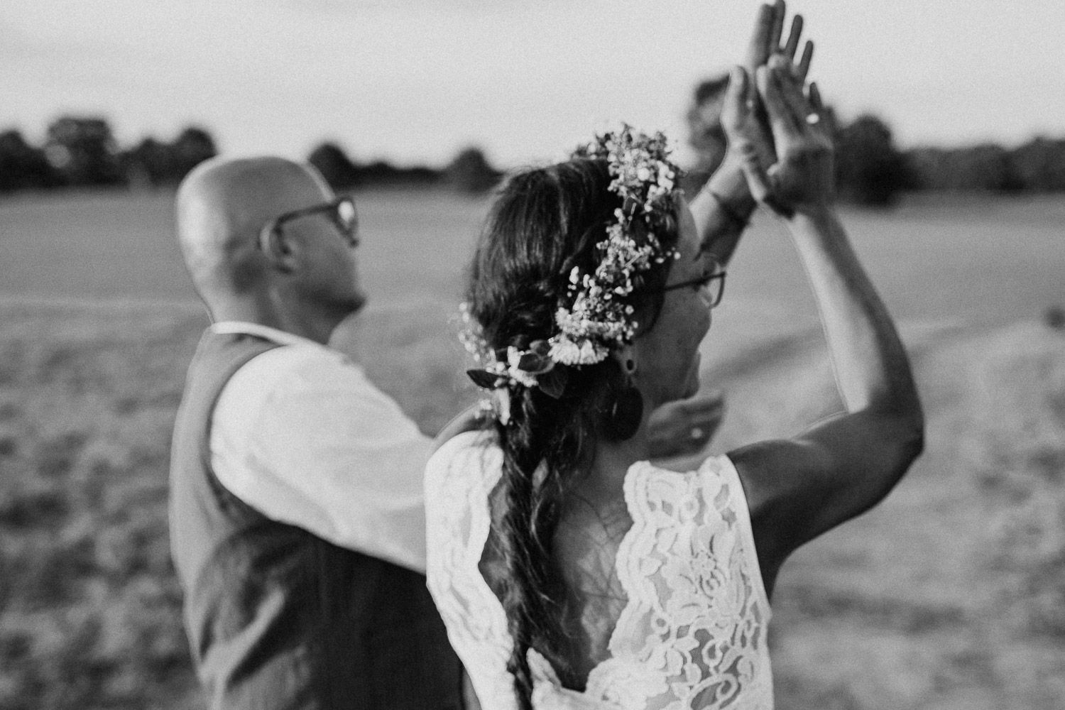 Black and white photo of bride with floral hair crown and lace dress dancing with groom in a field.