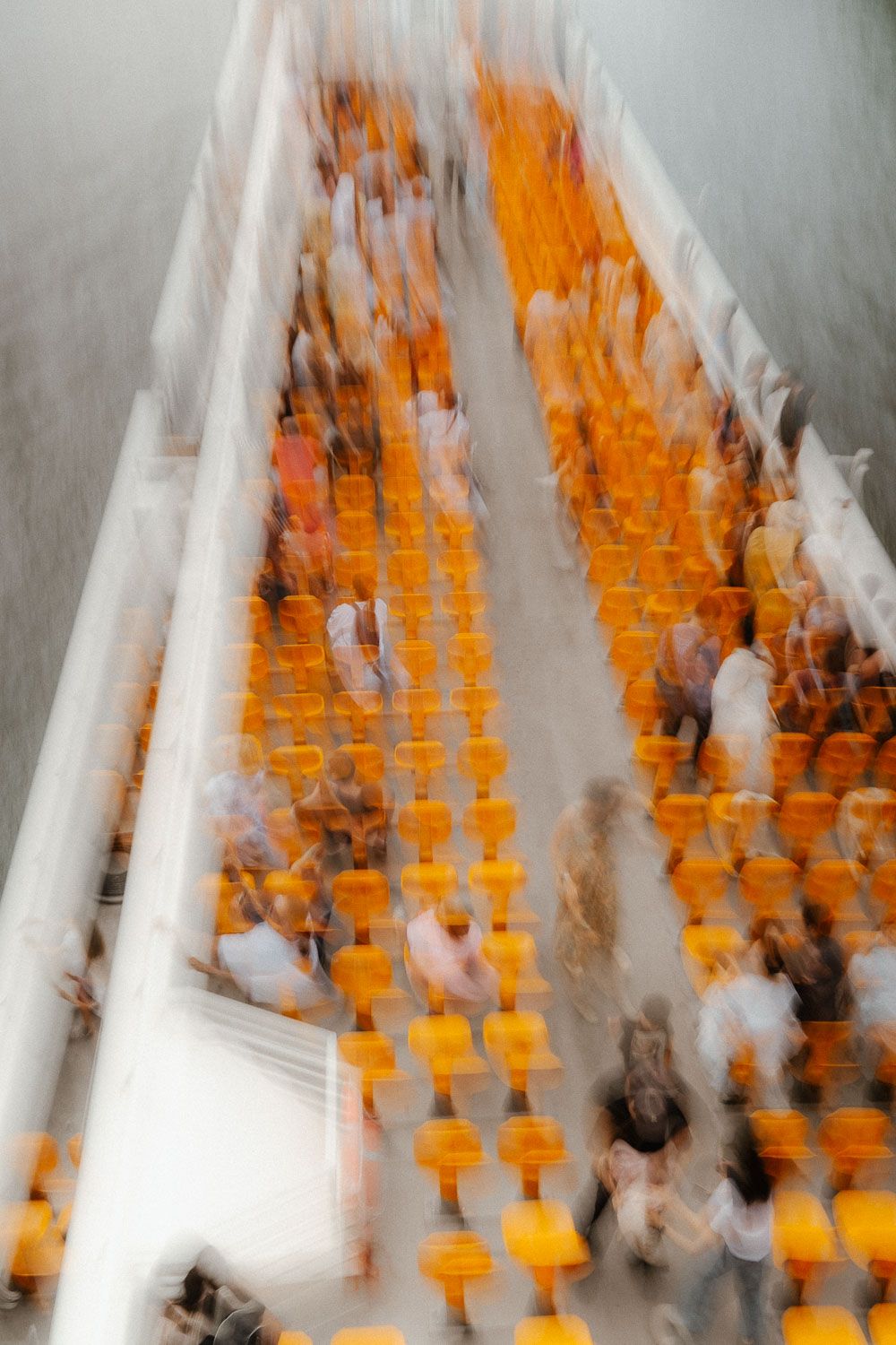 Motion blur aerial view of people seated in rows of orange chairs in a bright white modern auditorium.