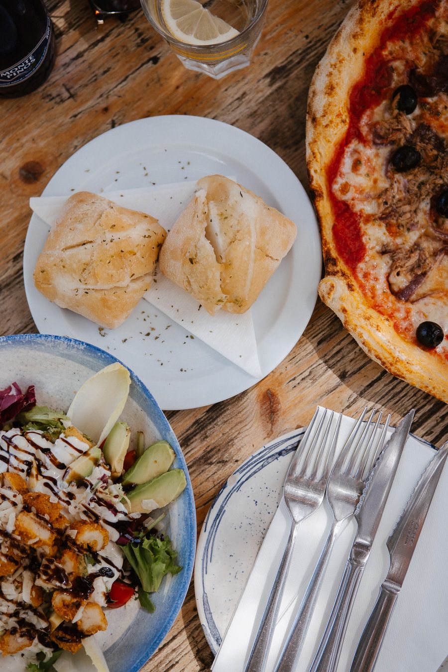 Overhead view of Italian meal with focaccia bread, pizza, and fresh salad on wooden table.