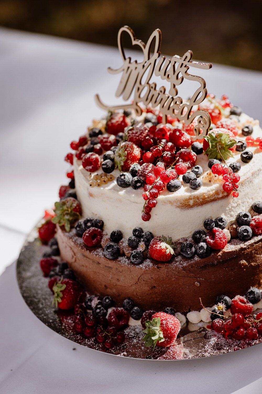 Two-tier chocolate wedding cake topped with fresh berries and a Just Married topper.