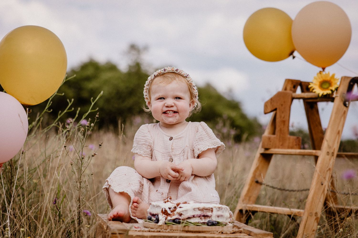 Happy toddler girl in pink dress celebrating first birthday with balloons.