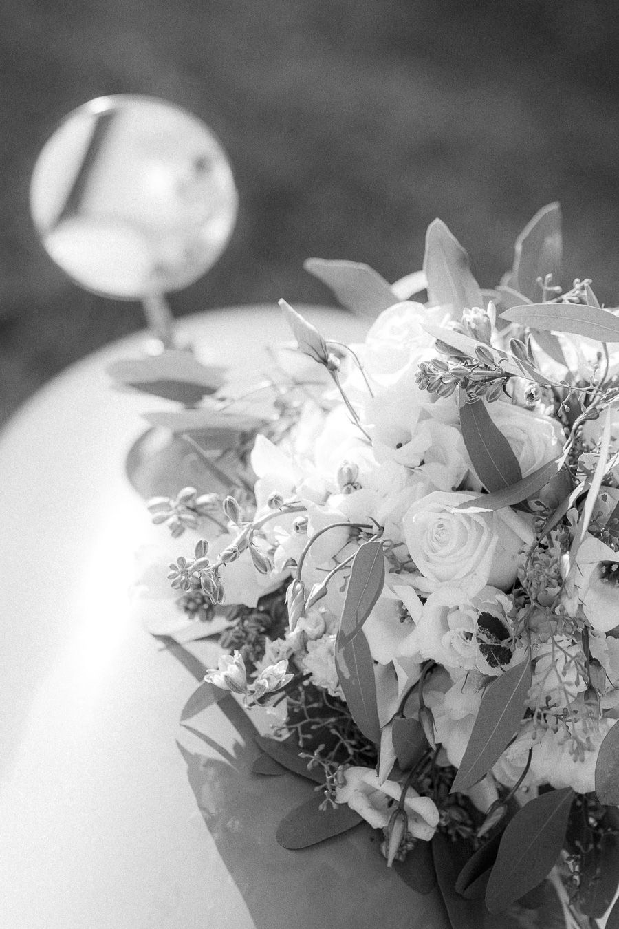 Black and white photo of a bridal bouquet with white roses and eucalyptus leaves on a car hood.