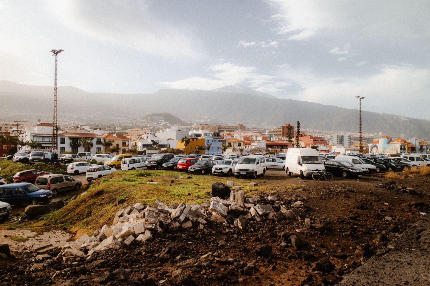 Panoramic view of a hillside town with parked vehicles and mountains under a cloudy dramatic sky.