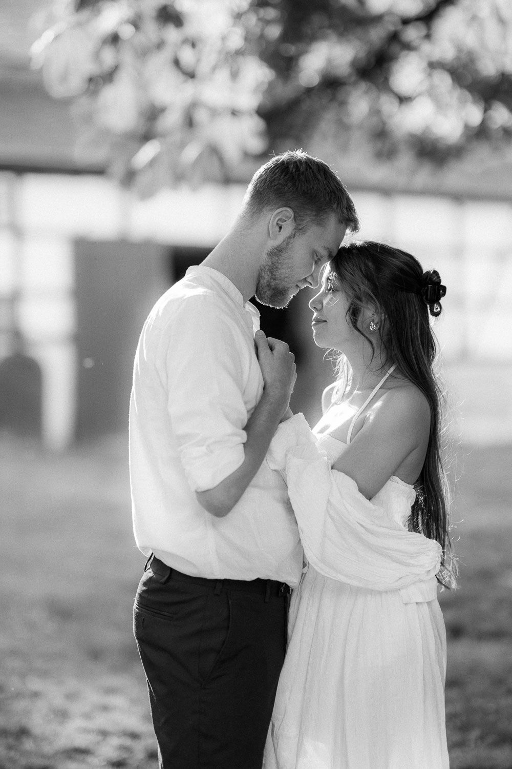 Black and white photo of a romantic couple embracing outdoors, groom in white shirt and bride in wedding dress.