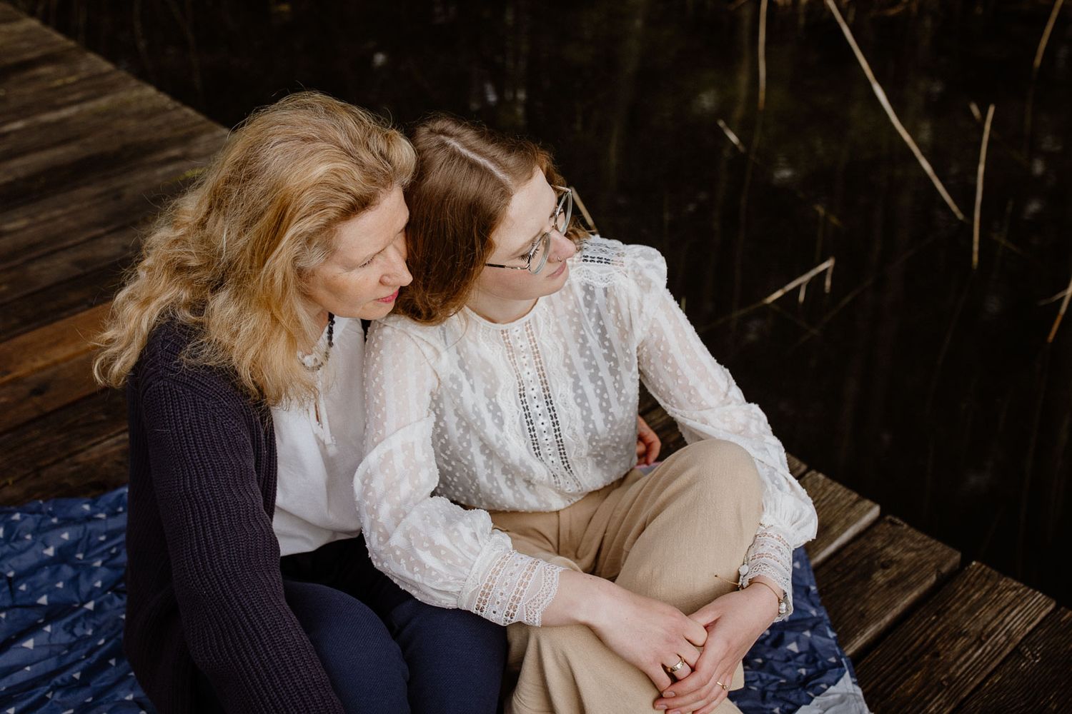 Mother and daughter sitting together on wooden dock near water.
