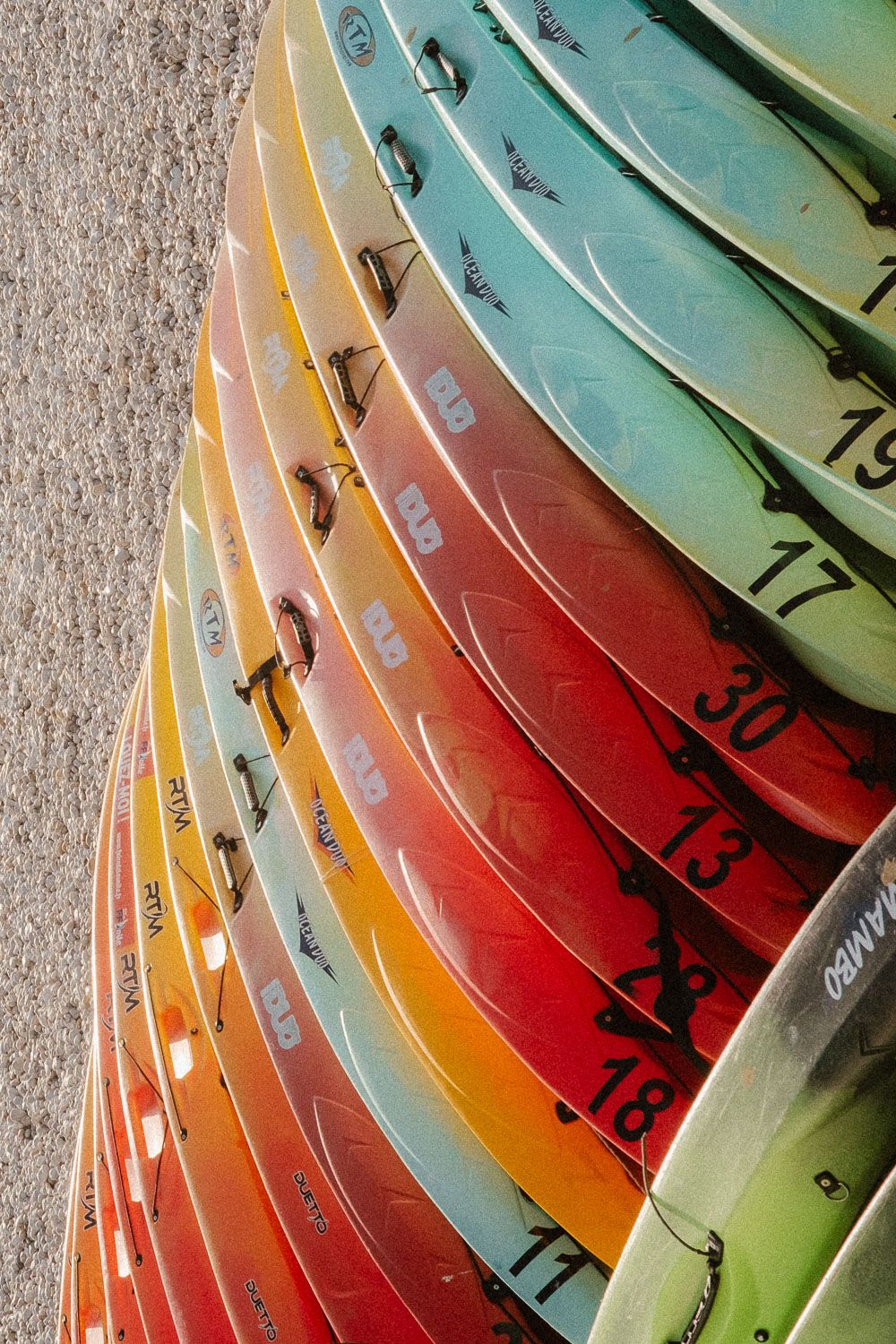 Colorful numbered kayaks stacked in a row displaying vibrant rainbow gradient of red, orange, and teal.