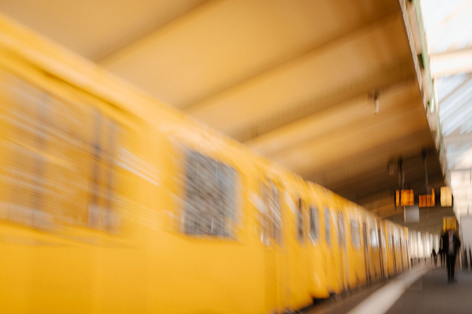 Motion blur of yellow Berlin U-Bahn subway train arriving at elevated station platform.