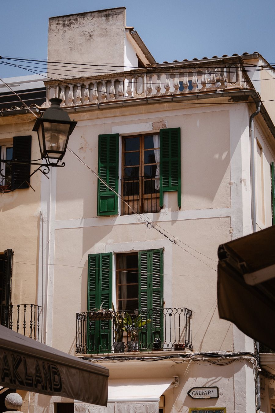 White Mediterranean building with green shuttered windows and wrought iron balcony under clear blue sky.