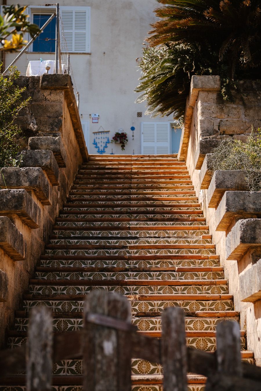 Ornate tiled staircase with stone balustrades leading up to a Mediterranean building with palm trees.