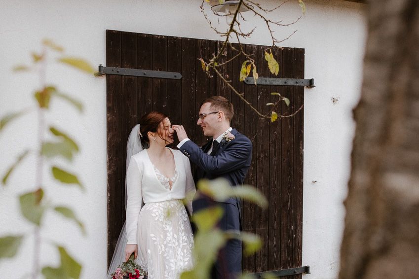 Bride and groom share tender moment laughing together in front of rustic wooden door.