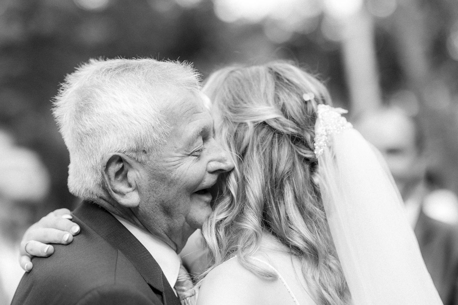 Black and white photo of an elderly man joyfully embracing a smiling bride at a wedding celebration.