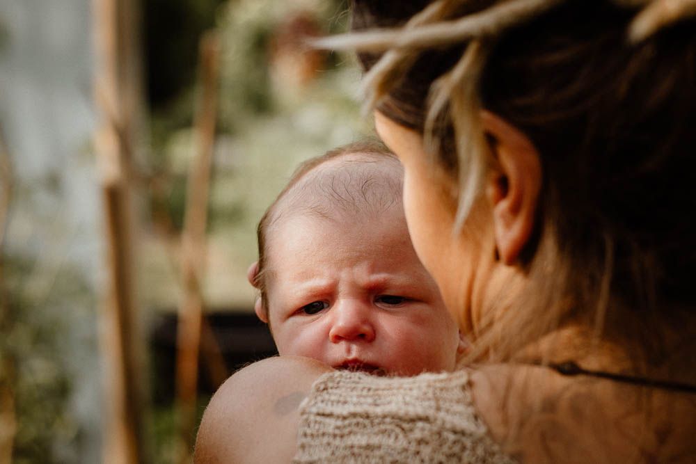 Mother tenderly holding a crying newborn baby outdoors in natural light.